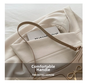 Close-up of beige underarm bag with gold bow hardware resting on a matching blazer