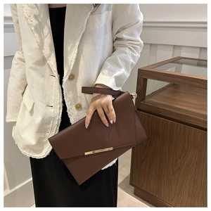 Detail of dark brown envelope clutch bag featuring a gold metal bar and leather wrist strap