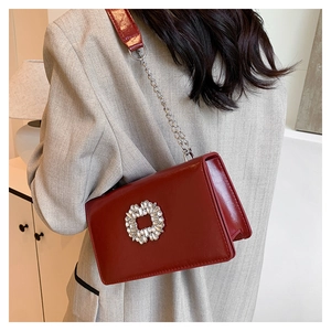 Détail d'un sac bandoulière rouge foncé avec boucle en strass et chaîne sur un modèle