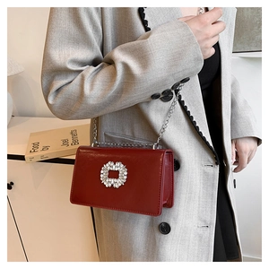 Détail du sac à bandoulière bordeaux avec boucle en strass porté sur un blazer gris