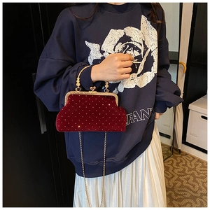Detail of red velvet evening bag with gold chain and pearl clasp held by a model