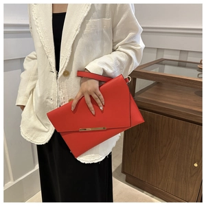 Detail of red faux leather envelope clutch with golden metal trim and wrist strap
