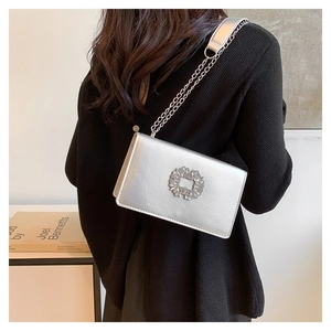 Petit sac carré argenté avec boucle en strass et bandoulière chaîne porté par un modèle