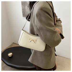 Chic cream-colored shoulder bag with gold bow clasp worn with a stylish brown blazer