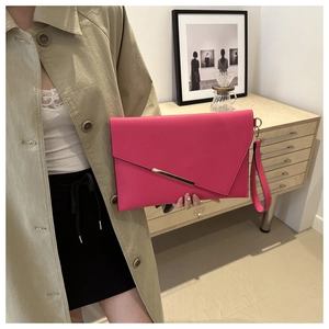 Detail of rose red envelope clutch bag with gold metal trim and detachable wrist strap