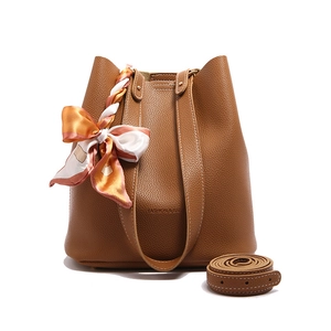 Brown litchi grain leather bucket bag with silk scarf and adjustable strap on white background