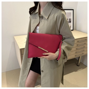 Detail of rose red envelope clutch bag with metal trim held by model in trench coat