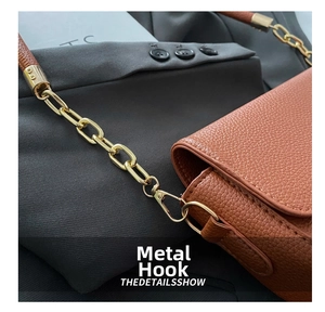 Close-up of golden metal hook and chain on brown lychee grain leather saddle bag