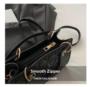 Detail view of the quilted black handbag featuring a gold metal handle and smooth zipper