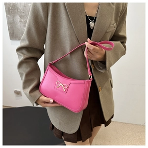 Detail of rose pink matte leather underarm bag with a golden metal bow accessory