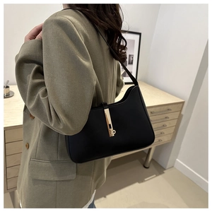 Chic black leather underarm bag with gold metal buckle shown in a lifestyle setting
