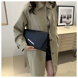 Detail of a black envelope clutch with silver metal trim held by a woman in a trench coat