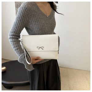 Detail of white envelope clutch bag with silver metal bow and wristlet strap