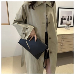 Detail of a chic black envelope clutch with gold metal trim held by a model in a trench coat