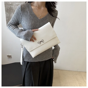 Close-up of white envelope clutch bag with metal bow detail and matching wrist strap