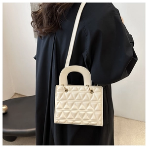 White mini handbag with triangle quilting worn by a model in a minimalist black dress