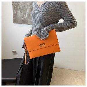 Close-up of orange envelope clutch bag with silver bow buckle held by a model