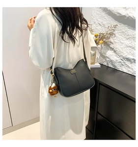 Detail of black leather hobo bag featuring a metal fashion tag and brown plush charm