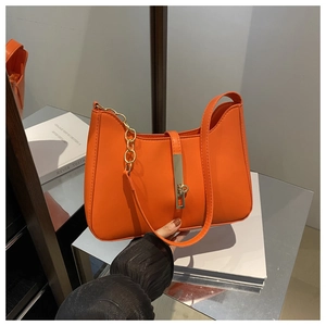 Detail of orange underarm bag featuring glossy texture and golden chain strap link
