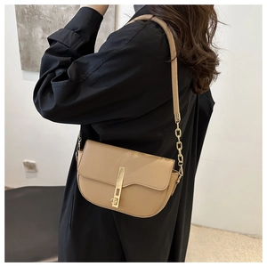 Close-up of khaki pebbled leather saddle bag with gold clasp on black coat