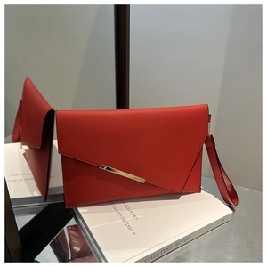 Detail of red leather clutch bag with asymmetrical flap and gold metal trim
