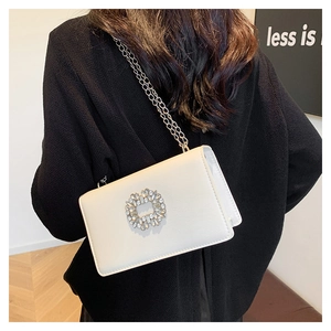 Détail du sac en cuir blanc avec boucle fleur en cristal et bandoulière chaîne argentée
