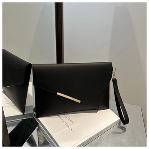 Detail of a sleek black envelope clutch bag with gold bar accent on a white book surface