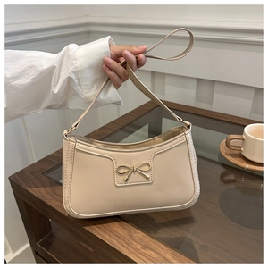 Dettaglio di una borsa baguette beige con fibbia metallica a forma di fiocco dorato