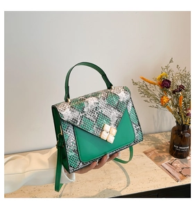 Detail of green and snake pattern shoulder bag with stone buckles held by a hand