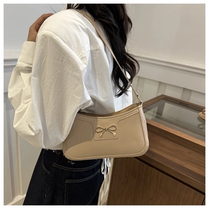 Dettaglio di una borsa sottobraccio beige in similpelle con fiocco in metallo decorativo