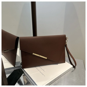 Close-up of brown leather envelope clutch with gold metal bar and wristlet strap