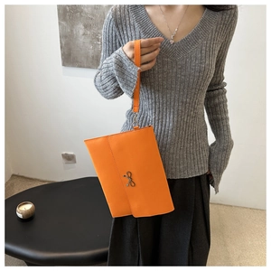 Close-up of bright orange envelope clutch featuring a metal bow and lychee grain texture