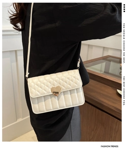 Detail of quilted beige shoulder bag with golden heart-shaped metal lock on the flap