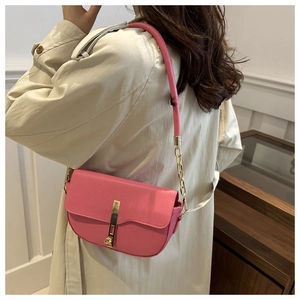 Detail of pink pebbled leather saddle bag with gold metal clasp on beige trench coat