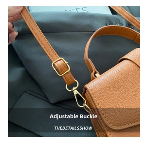 Detail of gold metal buckle and hook on brown litchi texture leather shoulder strap