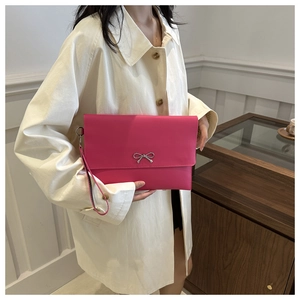 Detail of fuchsia envelope clutch bag with silver bow and wristlet strap on a model
