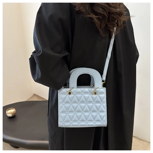 Detail of light blue quilted square handbag with matte gold hardware worn by a model