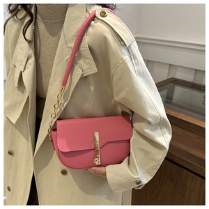 Detail of pink pebbled leather crossbody bag with gold metal buckle on beige trench coat