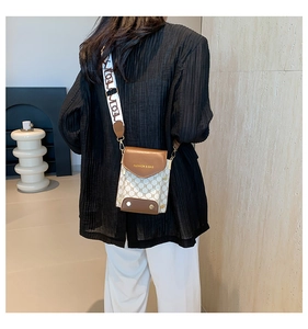 Detail of crossbody phone bag showing geometric texture, brown flap, and wide strap