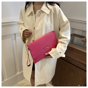Close-up of bright rose red clutch bag featuring a silver metal bow and wrist strap