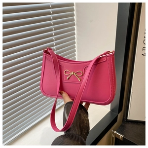 Detail of hot pink shoulder bag featuring a sleek leather finish and gold bow ornament