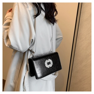 Détail d'un sac à bandoulière noir avec boucle en strass et fine bandoulière en chaîne