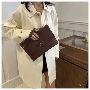 Detail of a brown leather envelope clutch with silver metal bow and wrist strap