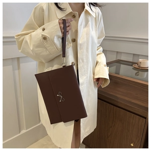 Close-up of a brown envelope clutch bag featuring a silver bow and detachable wrist strap
