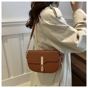 Detail of a brown leather saddle bag with a golden metal lock and elegant chain strap