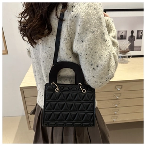 Detail of black quilted crossbody bag with triangular texture and gold metal rings