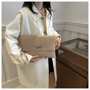 Chic beige bow envelope clutch with wrist strap held by model in elegant coat