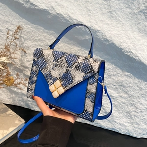 Minimalist crossbody bag with blue leather and snakeskin patchwork design held by hand