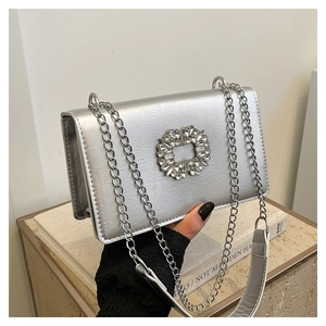Détail du sac à main argenté brillant avec une boucle circulaire ornée de strass