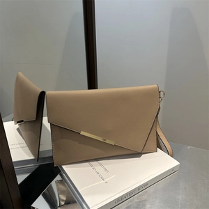 Elegant beige envelope flap crossbody bag with gold metal trim on white books